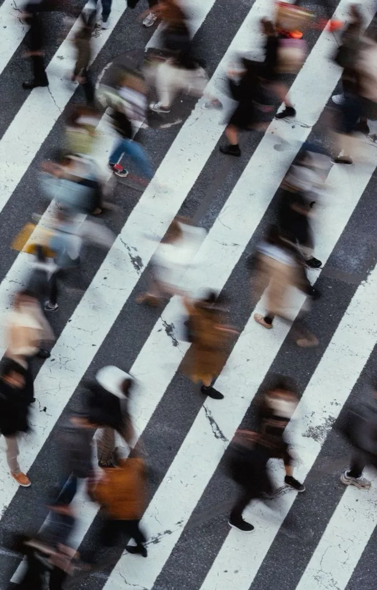 Overhead view of people crossing a striped crosswalk, blurred by motion, in grey and white.
